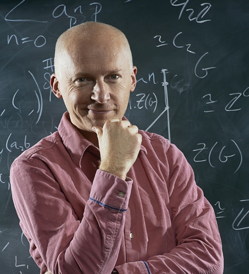 Marcus du Sautoy standing at blackboard with mathematical formulae and equations.